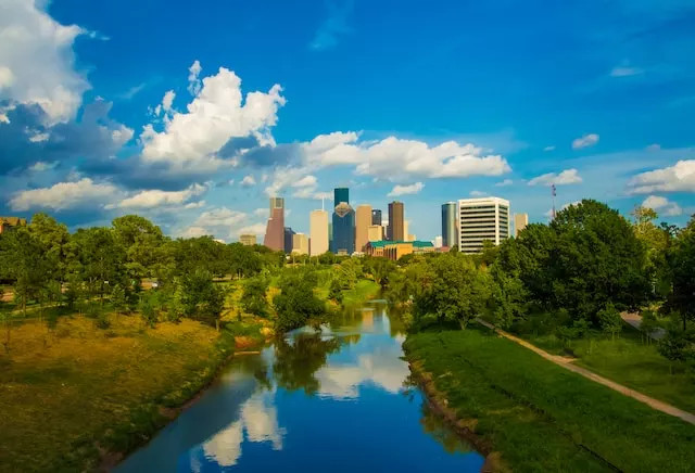 Houston: A Safe and Comfortable Destination for High-End Travelers. The image depicts green trees surrounding a body of water under a blue sky during the daytime.